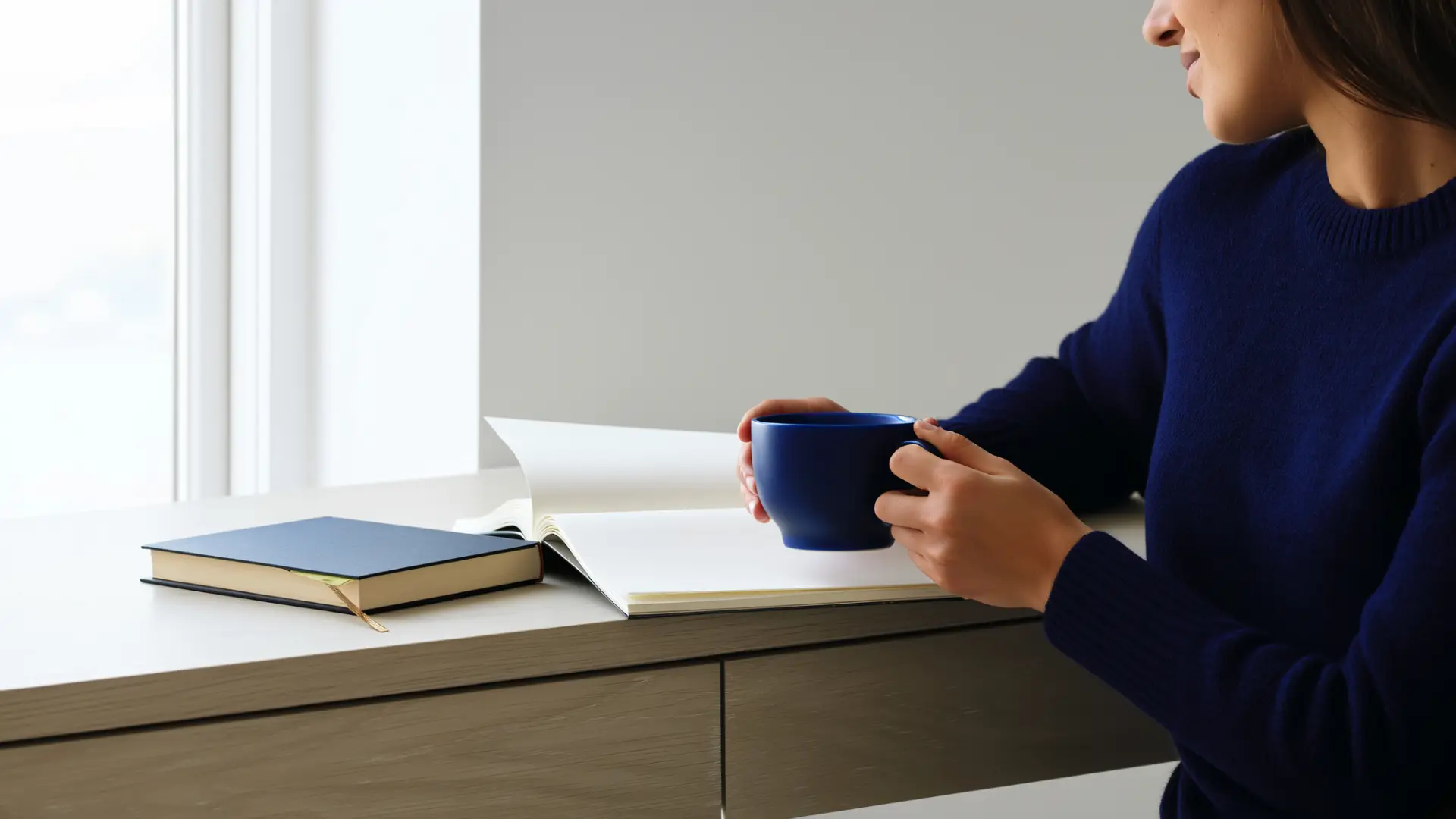 A person holding a mug beside an open notebook on a desk